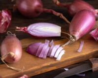 Sliced Red tropea onions with a knife on a wooden board close up. Traditional local south italian vegetable. Cooking process in home kitchen